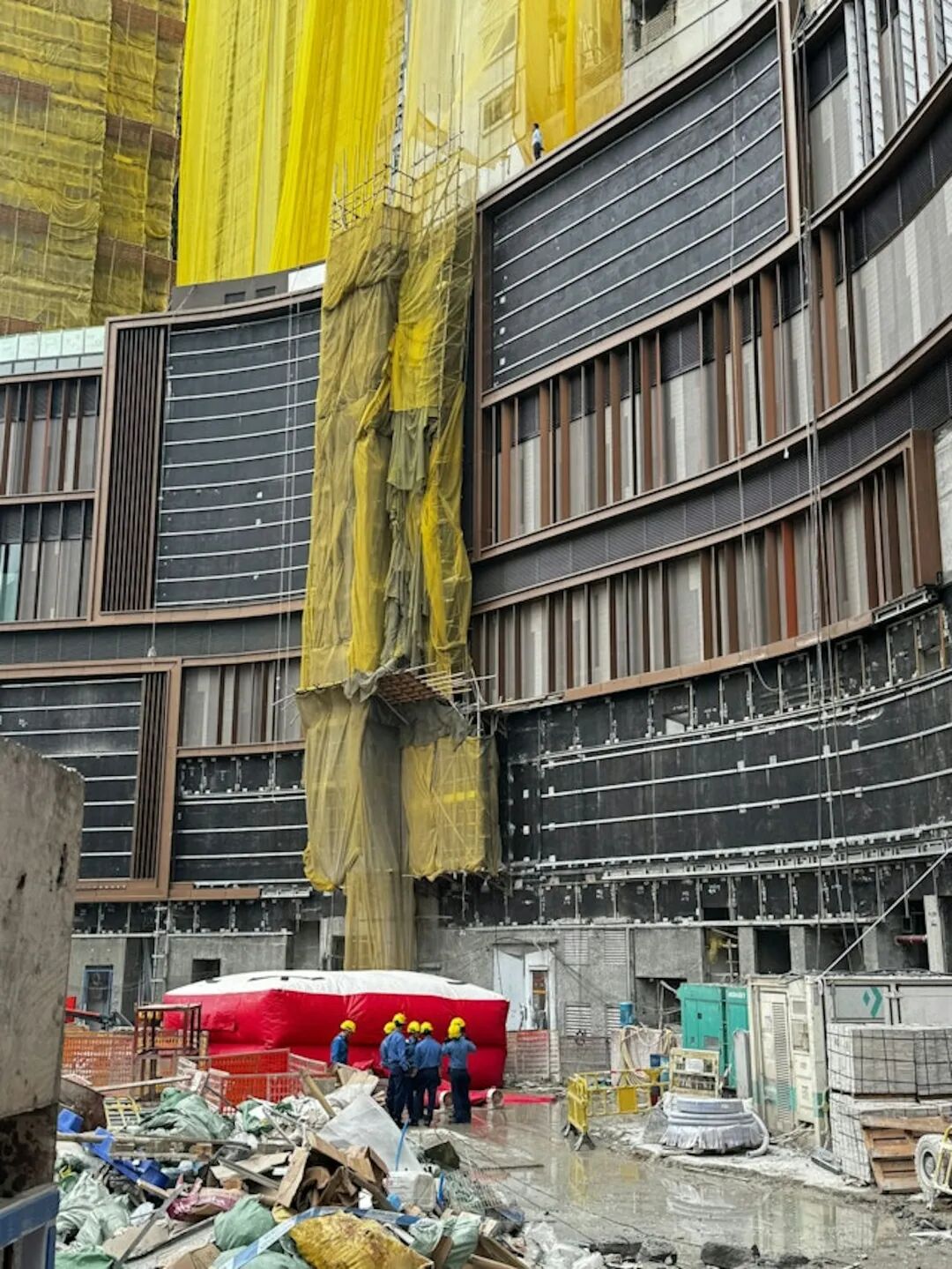 啟德房協地盤「啟點KEyPoint」懷疑拖欠工人薪金，本月17日，約30名工人在地盤外拉橫額，其間多人站在平台危險位置。消防員在場開氣墊。（讀者提供）